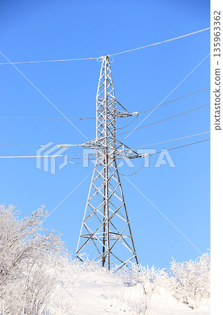 Winter landscape of Central Russia with an icy high-voltage power line. Beautiful trees covered in a thick layer of frost and snow in the bitter cold. A wonderful winter invitation card for tourists. Winter landscape of Central Russia with an icy high-voltage power line. Beautiful trees covered in a thick layer of frost and snow in the bitter cold. A wonderful winter invitation card for tourists. 135963362