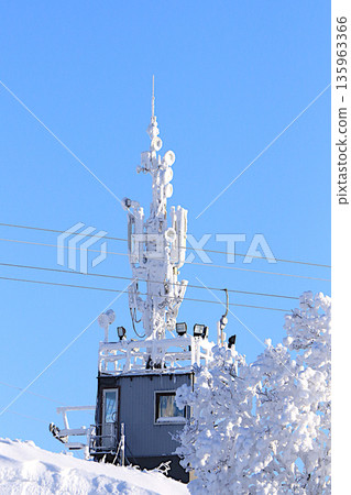 Winter landscape of Central Russia with an icy high-altitude antenna for communication with ice dishes and receivers. Beautiful trees covered with a thick layer of frost and snow in a severe frost. Winter landscape of Central Russia with an icy high-altitude antenna for communication with ice dishes and receivers. Beautiful trees covered with a thick layer of frost and snow in a severe frost. 135963366