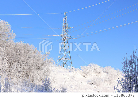 Winter landscape of Central Russia with an icy high-voltage power line. Beautiful trees covered in a thick layer of frost and snow in the bitter cold. A wonderful winter invitation card for tourists. Winter landscape of Central Russia with an icy high-voltage power line. Beautiful trees covered in a thick layer of frost and snow in the bitter cold. A wonderful winter invitation card for tourists. 135963372