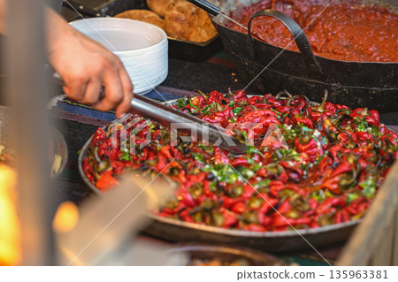 Roasted Red Peppers at Food Counter. Tray of roasted red peppers mixed with herbs and garlic at a food counter. Concept of food preparation, catering, meal service Roasted Red Peppers at Food Counter. Tray of roasted red peppers mixed with herbs and garlic at a food counter. Concept of food preparation, catering, meal service 135963381