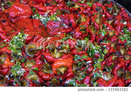 Roasted red peppers with herbs and garlic. Tray of roasted red peppers mixed with herbs and garlic in food preparation setting. Concept of food preparation, cuisine, meal ingredients 135963382