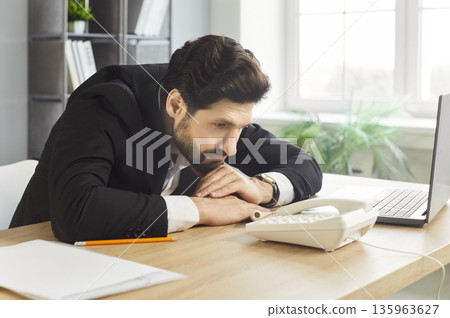Businessman waiting for a phone call at office desk, bored and frustrated Businessman waiting for a phone call at office desk, bored and frustrated 135963627