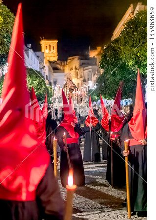 Many nazarenos with red hoods walking in procession Many nazarenos with red hoods walking in procession 135963659