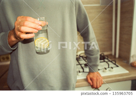 Man is holding glass of water with lemon slice in it. Concept of health and wellness. 135963705