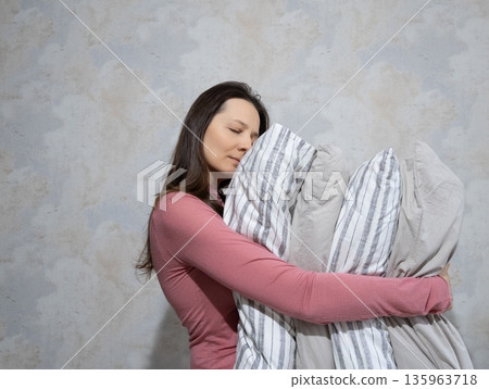 woman holds pile of pillows in her hands. pillows are in different colors, look like stack. woman holds pile of pillows in her hands. pillows are in different colors, look like stack. 135963718