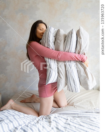 woman holds pile of pillows in her hands. pillows are in different colors, look like stack. woman holds pile of pillows in her hands. pillows are in different colors, look like stack. 135963720