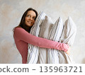 woman holds pile of pillows in her hands. pillows are in different colors, look like stack.  135963721