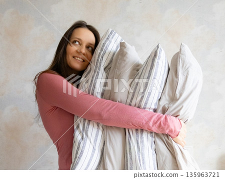 woman holds pile of pillows in her hands. pillows are in different colors, look like stack. woman holds pile of pillows in her hands. pillows are in different colors, look like stack. 135963721
