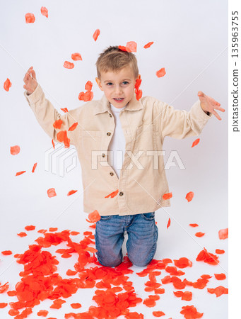 Little boy kneeling and throwing red petals into the air on white background. Valentines Day, fun, love, childhood happiness Little boy kneeling and throwing red petals into the air on white background. Valentines Day, fun, love, childhood happiness 135963755