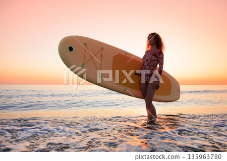 Young woman standing on beach with paddle sup boards during summer vacation 135963780