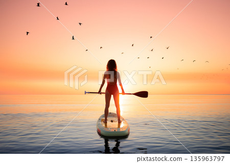 Young woman walking on stand up paddle sup boards by the sea during summer vacation Young woman walking on stand up paddle sup boards by the sea during summer vacation 135963797
