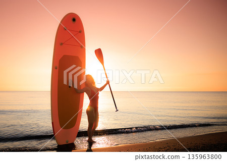 Young woman standing with stand up paddle sup boards by the sea during summer vacation Young woman standing with stand up paddle sup boards by the sea during summer vacation 135963800