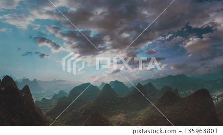 Scenic view of Yangshuo's distinctive cone shaped limestone mountains. Vibrant blue sky contrasts with green forested peaks. Classic Chinese landscape scenery showcasing natural beauty and tourism 135963801