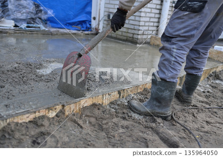 Worker Pouring and Spreading Fresh Concrete Slab in Formwor  135964050
