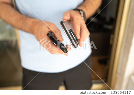 Close-up of a man holding a smartphone and a transparent protective case, preparing to put the case on the phone. 135964117