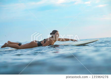 Teenage Woman Practicing On Surfboard At Calm Seaside Evening Teenage Woman Practicing On Surfboard At Calm Seaside Evening 135964278