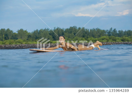 Young Woman Maintains Steady Stance During Evening Paddleboarding Session 135964289