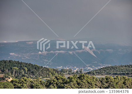 Dense green forest covering a mountain hillside, photographed from the road in August 2025, with layered trees, summer foliage, and a clear blue sky. Dense green forest covering a mountain hillside, photographed from the road in August 2025, with layered trees, summer foliage, and a clear blue sky. 135964376