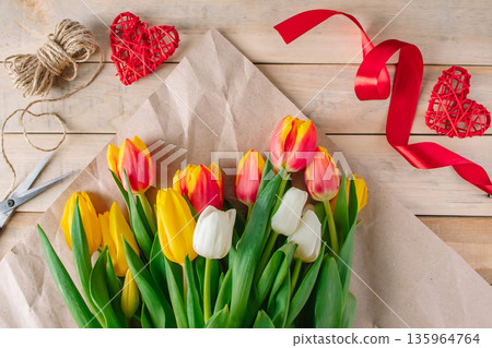 Florist woman wraps large bouquet of multi-colored tulips in eco-friendly craft paper. 135964764