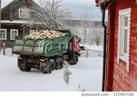 Firewood delivery truck turns onto driveway of rural house in snowy winter village. Firewood delivery truck turns onto driveway of rural house in snowy winter village. 135965598