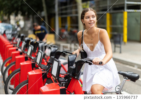 Young girl taking red bicycle from Bicing rental station Young girl taking red bicycle from Bicing rental station 135966737