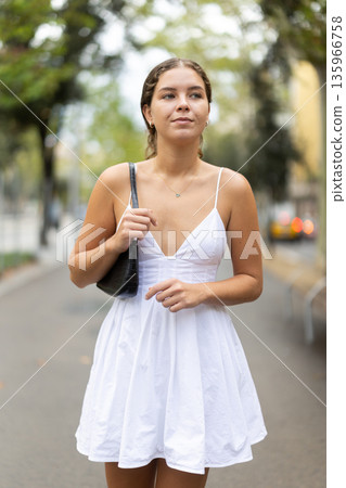 Young girl in white summer dress walking along quiet city street Young girl in white summer dress walking along quiet city street 135966758