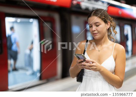 Young woman standing on platform near train with mobile phone Young woman standing on platform near train with mobile phone 135966777