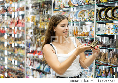 Smiling girl choosing architectural landmark figurine in souvenir shop Smiling girl choosing architectural landmark figurine in souvenir shop 135966788