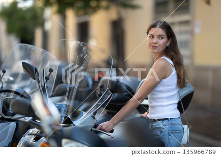 Young girl standing by scooter on city street Young girl standing by scooter on city street 135966789