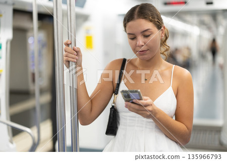 Calm young girl scrolling phone while standing on wagon Calm young girl scrolling phone while standing on wagon 135966793