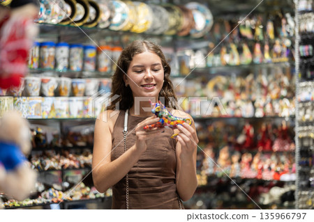 Nice young girl tourist choosing traditional spanish ceramic figurine as gift in souvenir market 135966797