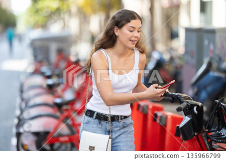 Young woman unlocking rental bike for city ride Young woman unlocking rental bike for city ride 135966799