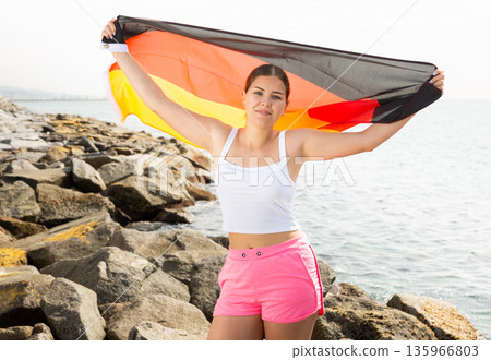Young woman on coast posing with flag of Germany Young woman on coast posing with flag of Germany 135966803