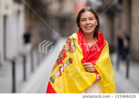 Patriotic young woman waving the flag of Spain on city street 135966828