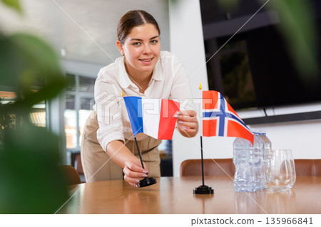 Young female assistant putting up norwegian and french flags on table for international negotiations Young female assistant putting up norwegian and french flags on table for international negotiations 135966841