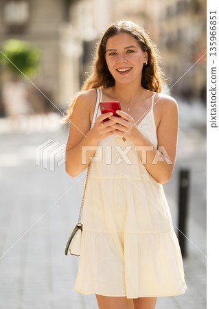 Happy young woman with mobile phone in her hands walking around city and taking pictures of sights Happy young woman with mobile phone in her hands walking around city and taking pictures of sights 135966851