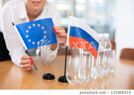 Unrecognizable girl sets midget flags of Russia and European Union before international negotiations Unrecognizable girl sets midget flags of Russia and European Union before international negotiations 135966910
