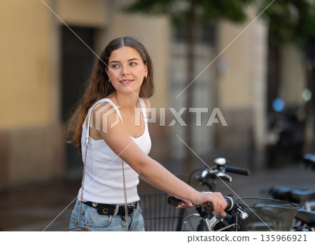 Young girl parks her bicycle on street after walking around city Young girl parks her bicycle on street after walking around city 135966921