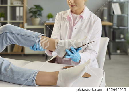 Cheerful female orthopedist fitting insole on patient's foot lying on couch in medical clinic. 135966925