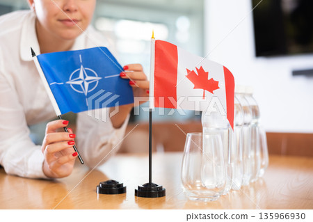 Unrecognizable girl sets midget flags of Canada and NATO before international negotiations 135966930