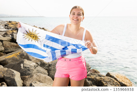 Young woman on coast posing with flag of Uruguay Young woman on coast posing with flag of Uruguay 135966938