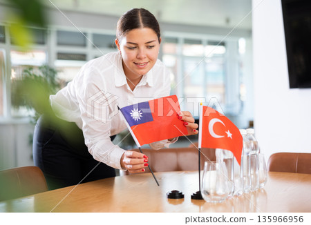 Positive young woman putting little flag of Taiwan on table next to the flag of Turkey Positive young woman putting little flag of Taiwan on table next to the flag of Turkey 135966956