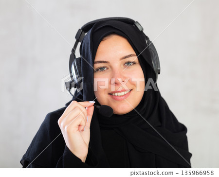 Happy young woman dressed in traditional islamic clothes with headphones with microphone on Happy young woman dressed in traditional islamic clothes with headphones with microphone on 135966958