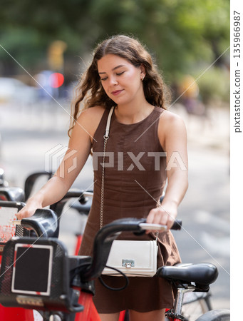 Stylish young girl looking to rent bike while walking through streets of Barcelona Stylish young girl looking to rent bike while walking through streets of Barcelona 135966987