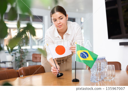 Young female assistant putting up brazilian and japanese flags on table for international negotiations Young female assistant putting up brazilian and japanese flags on table for international negotiations 135967007