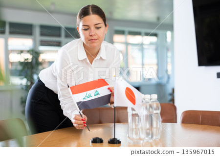 Female office coordinator placing flags of Iraq and Japan on table Female office coordinator placing flags of Iraq and Japan on table 135967015