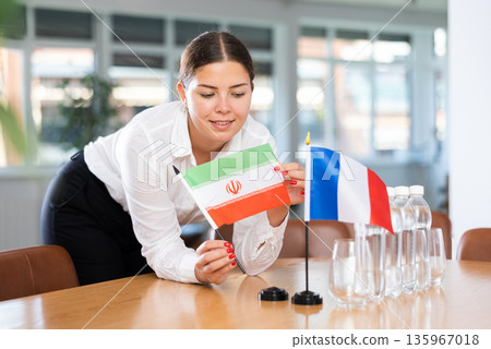 Woman secretary prepares the negotiating table - arranges flags of France and Iran Woman secretary prepares the negotiating table - arranges flags of France and Iran 135967018