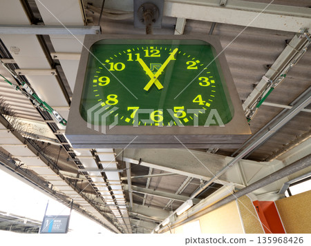 A green hanging analog clock installed on the station platform 135968426