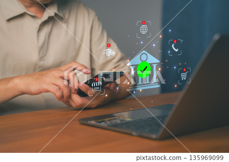 Man using smartphone and laptop with online banking icon, symbolizing digital finance, mobile payment, secure transaction. Shopping online, e-commerce, or financial technology connection concepts. Man using smartphone and laptop with online banking icon, symbolizing digital finance, mobile payment, secure transaction. Shopping online, e-commerce, or financial technology connection concepts. 135969099
