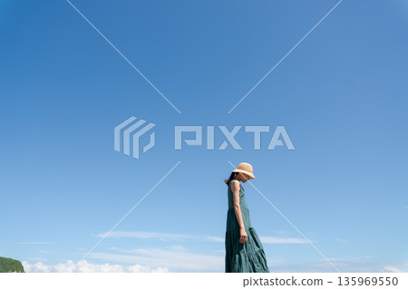 A young woman in a one-piece dress against the blue sky A young woman in a one-piece dress against the blue sky 135969550